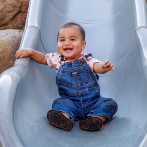Happy baby riding down a slide at the park